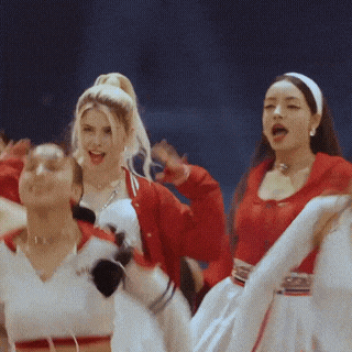 a group of women are dancing and one of them is wearing a white shirt that says ' aaa ' on it