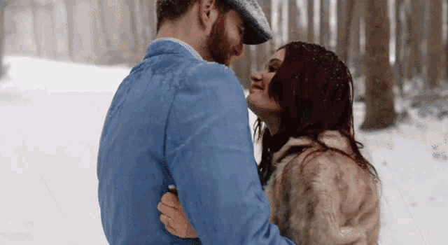 a man and a woman are kissing in the snow . the woman is wearing a fur coat .