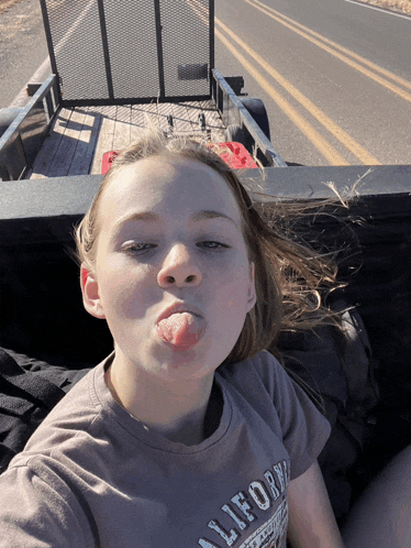 a girl wearing a california t-shirt sticks her tongue out