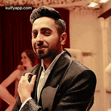 a man in a suit is smiling and adjusting his tie while standing in a room .