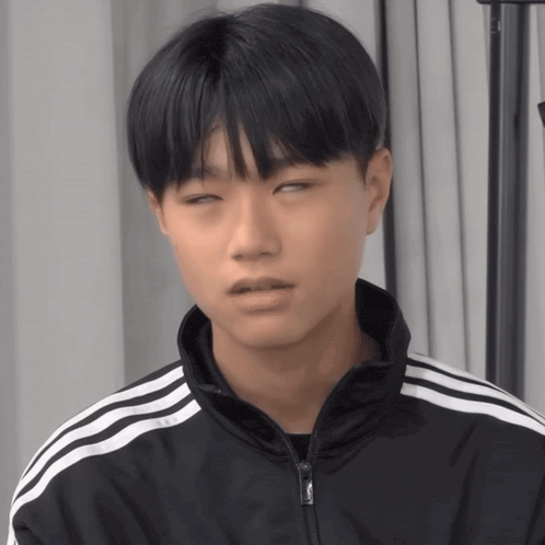 a young man wearing a black jacket with white stripes on the sleeves is making a funny face