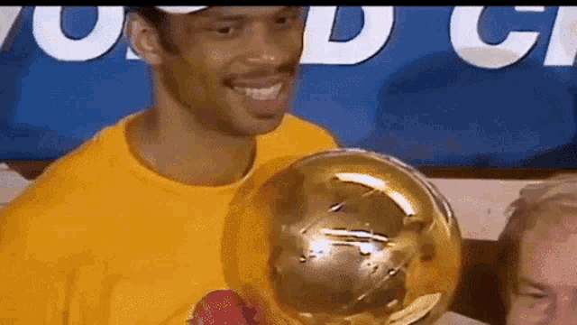 a man in a yellow shirt is holding a basketball trophy and smiling .