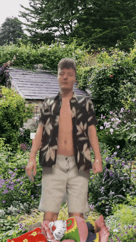 a shirtless man stands in a garden with flowers