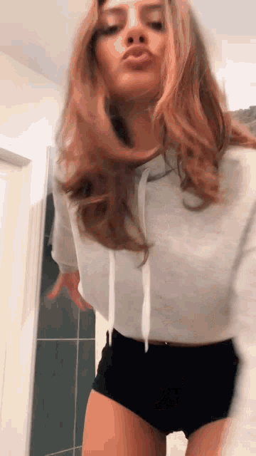 a woman in a white hoodie and black shorts is dancing in a room .