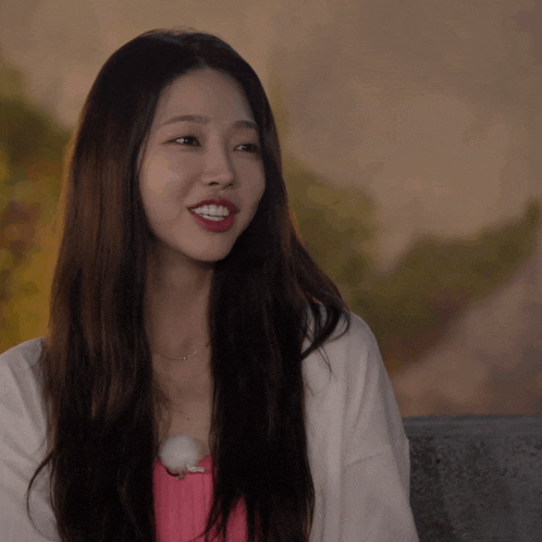 a woman with long dark hair is smiling and wearing a pink tank top