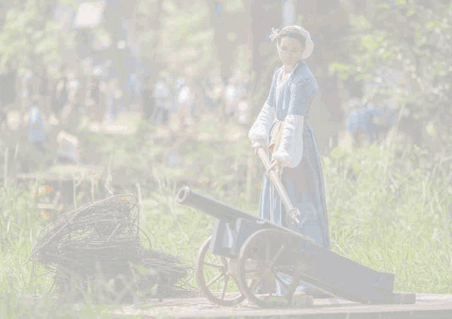 a woman in a blue dress is pushing a cannon in a field