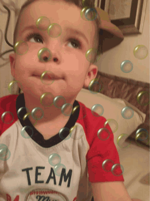 a little boy wearing a team shirt is surrounded by bubbles
