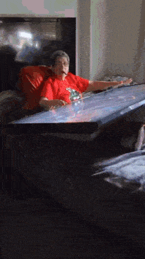 a man in a red shirt is laying on a bed holding a large flat screen television