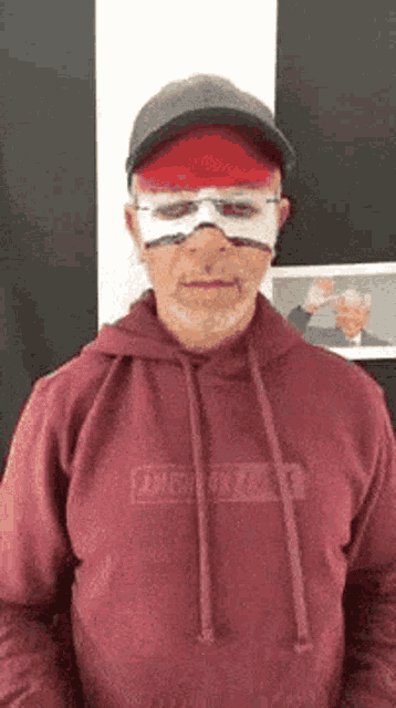 a man wearing a red hoodie and a hat is wearing a mask .