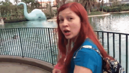 a woman with red hair is standing in front of a pond with a swan statue in the background .