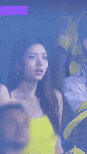 a woman in a yellow tank top stands in front of a purple banner that says hindiastar