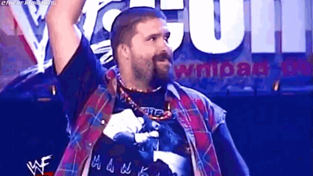 a man with a beard is wearing a plaid shirt and holding his arms up in the air .