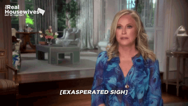 a woman in a blue shirt is standing in front of a living room with a sign that says real housewives