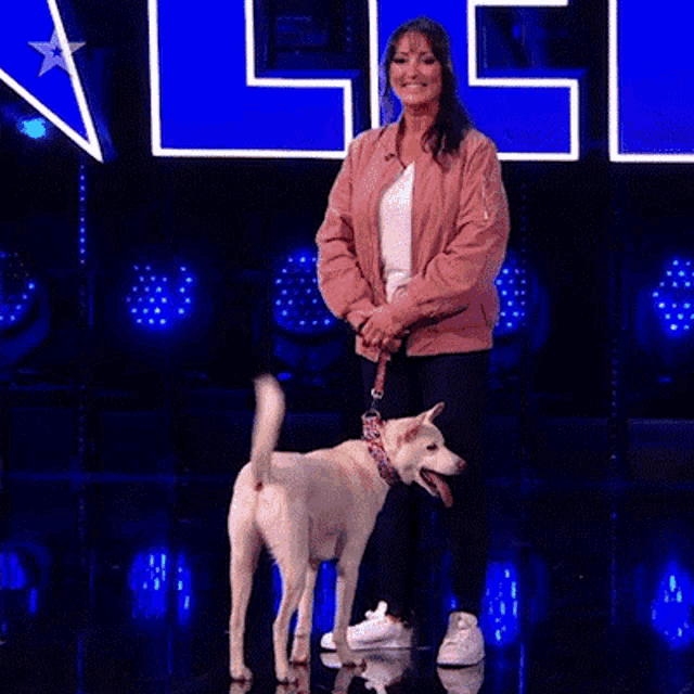 a woman in a pink jacket is standing next to a white dog on a stage .