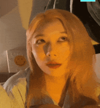 a woman with blonde hair looks at the camera in front of a smiley face