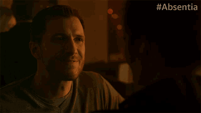 a man is smiling in a dark room with #absentia written in the corner