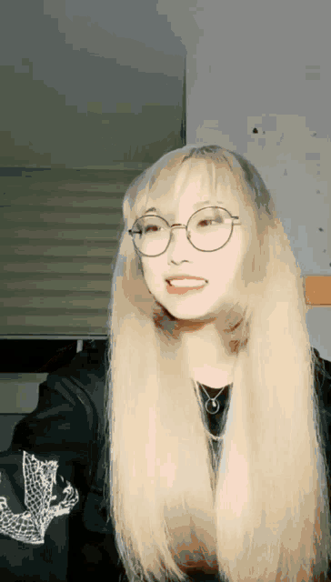 a girl with long blonde hair wearing glasses and a black jacket
