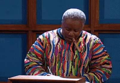 a man in a colorful sweater is sitting at a table with a cigar in his mouth .