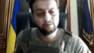 a man with a beard is sitting in front of a flag .