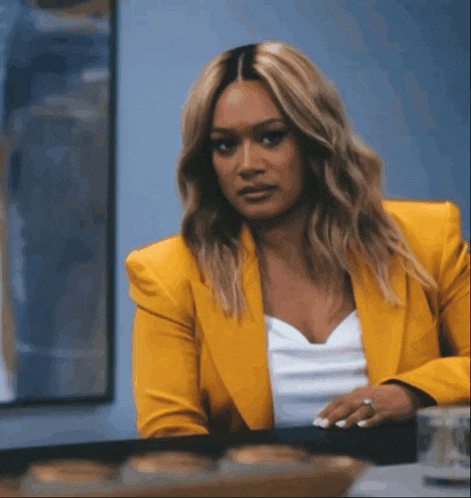a woman wearing a yellow jacket and a white shirt is sitting at a table