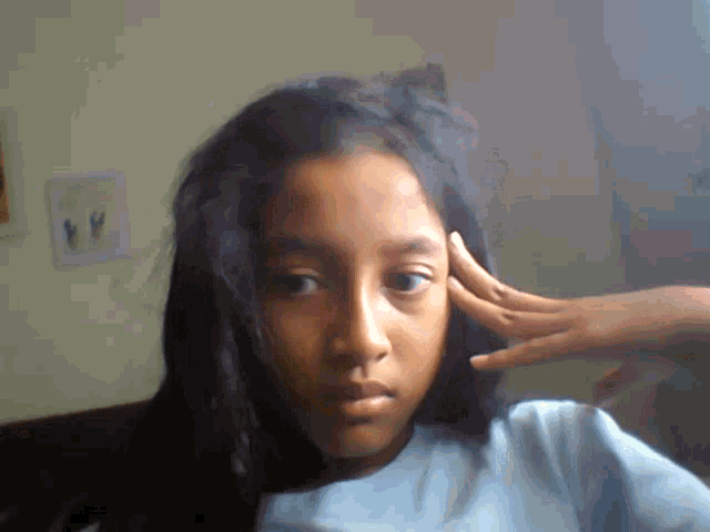 a girl 's hand rests on her forehead while looking at the camera