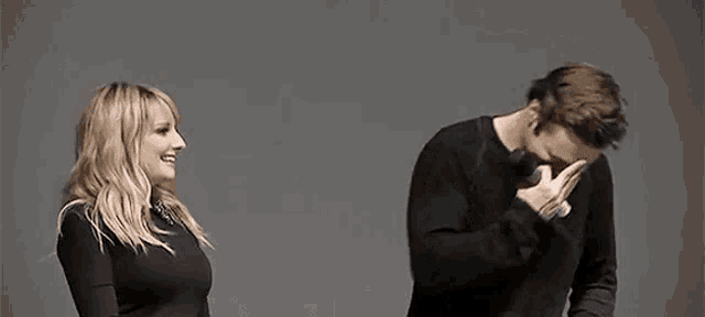 a man and a woman are standing next to each other on a stage . the man is covering his face with his hand .