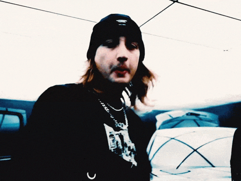 a man with long hair wearing a black beanie and a black shirt with a picture of a man on it