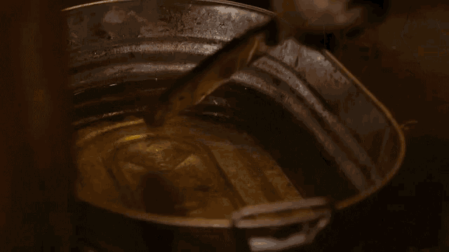 a person is holding a knife in a metal bucket of oil .