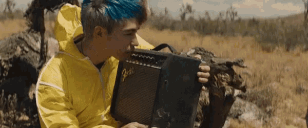 a man in a yellow jacket holds a fender amplifier