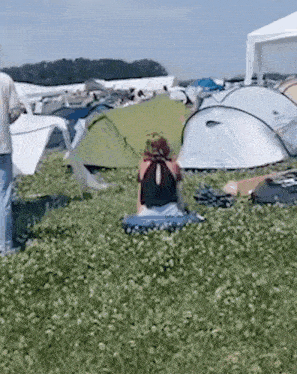 a woman is sitting in a field with tents