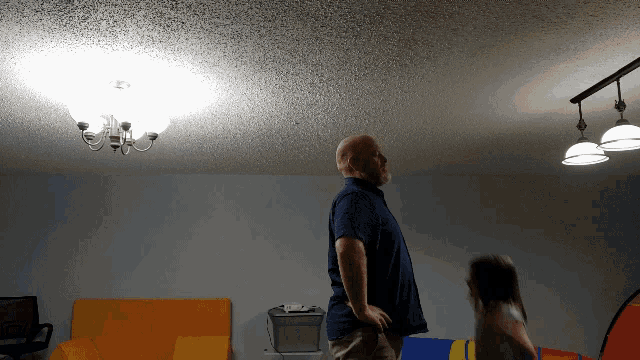 a man in a blue shirt stands in a room with a chandelier hanging from the ceiling