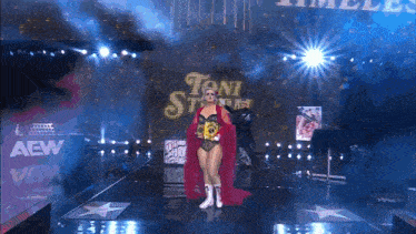 a woman in a red cape is walking down a stage with a sign that says aew on it