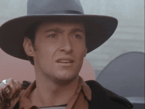 a man wearing a cowboy hat looks at the camera with a serious look on his face