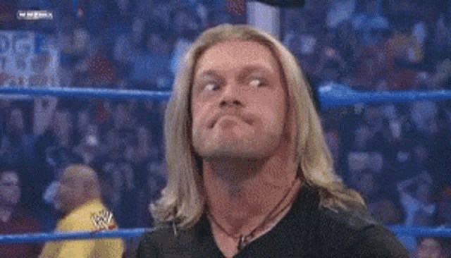 a wrestler with long blonde hair is standing in a wrestling ring .