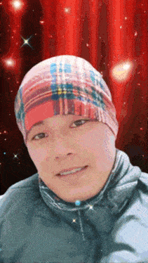 a man wearing a plaid beanie is smiling in front of a red curtain