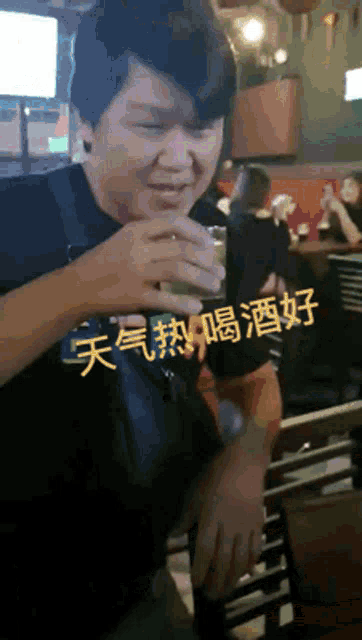 a man in a black shirt is drinking from a small glass with chinese writing on it
