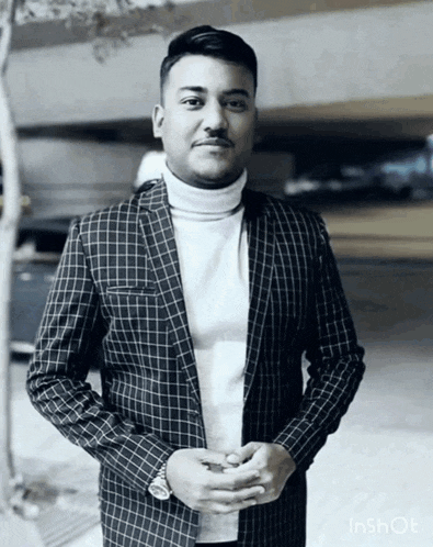 a man wearing a plaid jacket and a white turtleneck poses for a photo