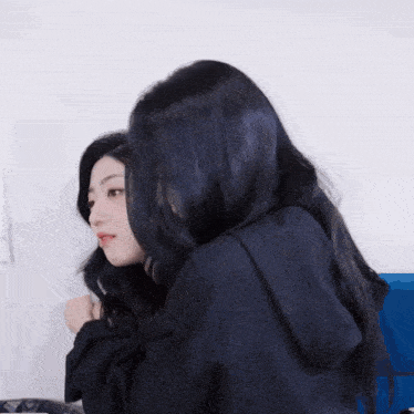 a woman with long black hair is hugging another woman with shorter black hair