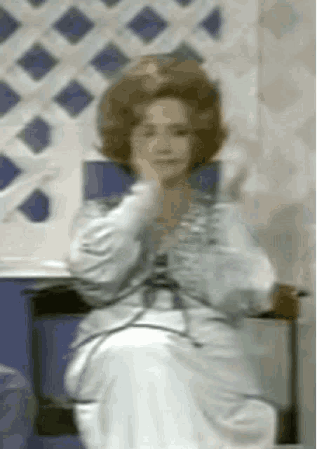 a woman in a white dress is sitting on a chair with her hands on her face .