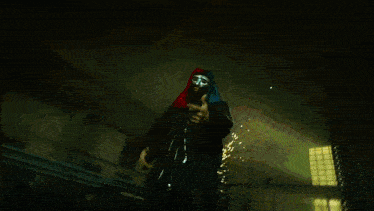 a man in a hooded jacket is standing in the dark holding a gun