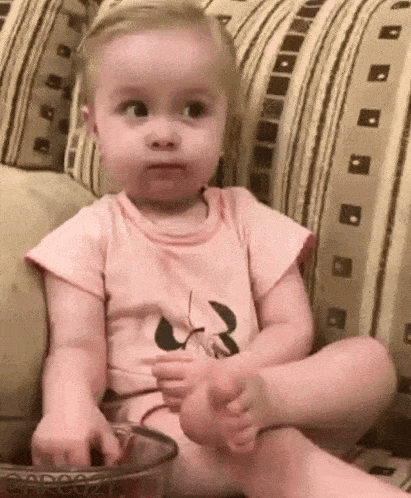 a baby girl is sitting on a couch with her feet up and making a face .