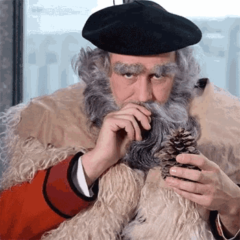 a man with a beard wearing a black hat holds a pine cone