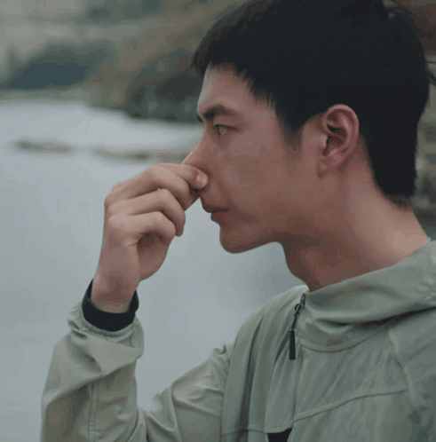 a man in a green jacket holds his nose