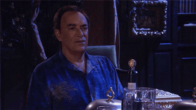 a man in a blue shirt sits at a table with a bottle of wine on it