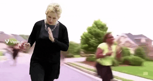 a woman in a black sweater is running down a street while a woman in a green shirt is running behind her .