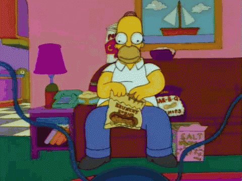 homer simpson from the simpsons is sitting on a couch eating a bag of chips .