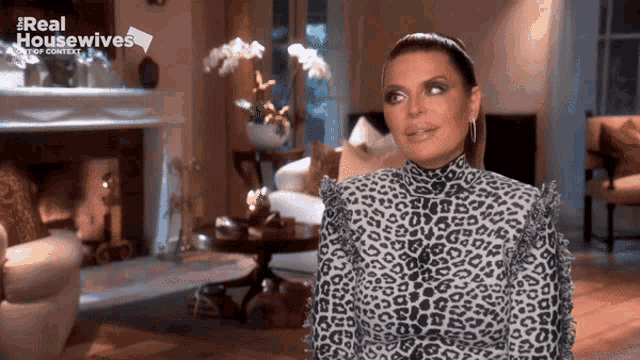 a woman in a leopard print top is sitting in a living room with a sign that says real housewives top context