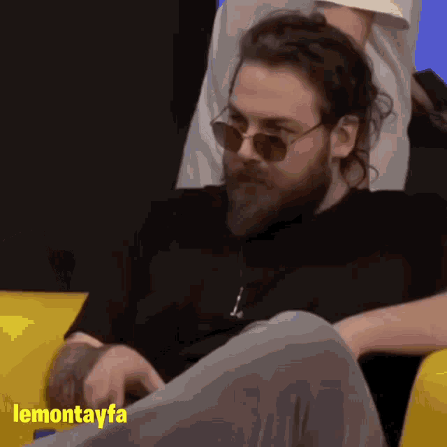 a man with a beard and sunglasses sits on a yellow couch