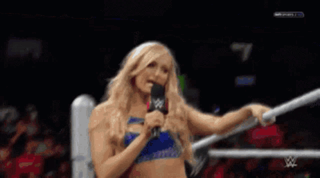 a woman is standing in a wrestling ring holding a microphone in front of an event sign
