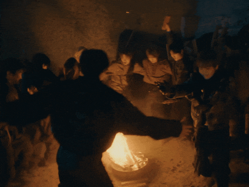 a group of people are standing around a fire